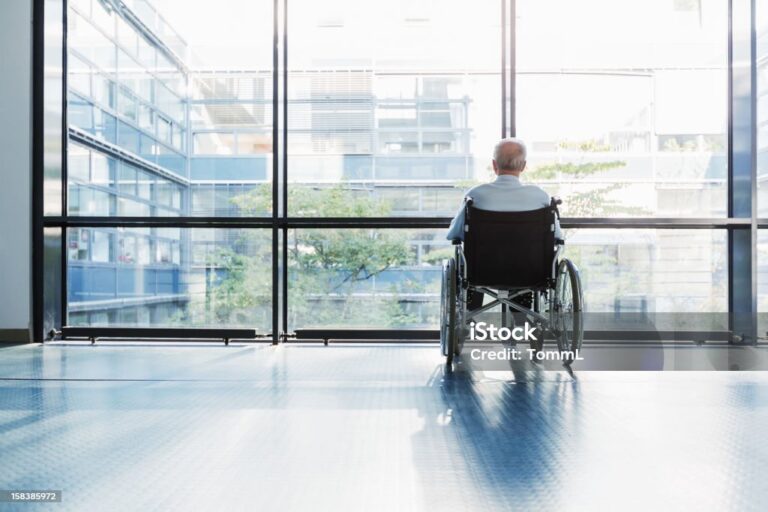 Senior Man in Wheelchair looking out of a window in a hospital corridor